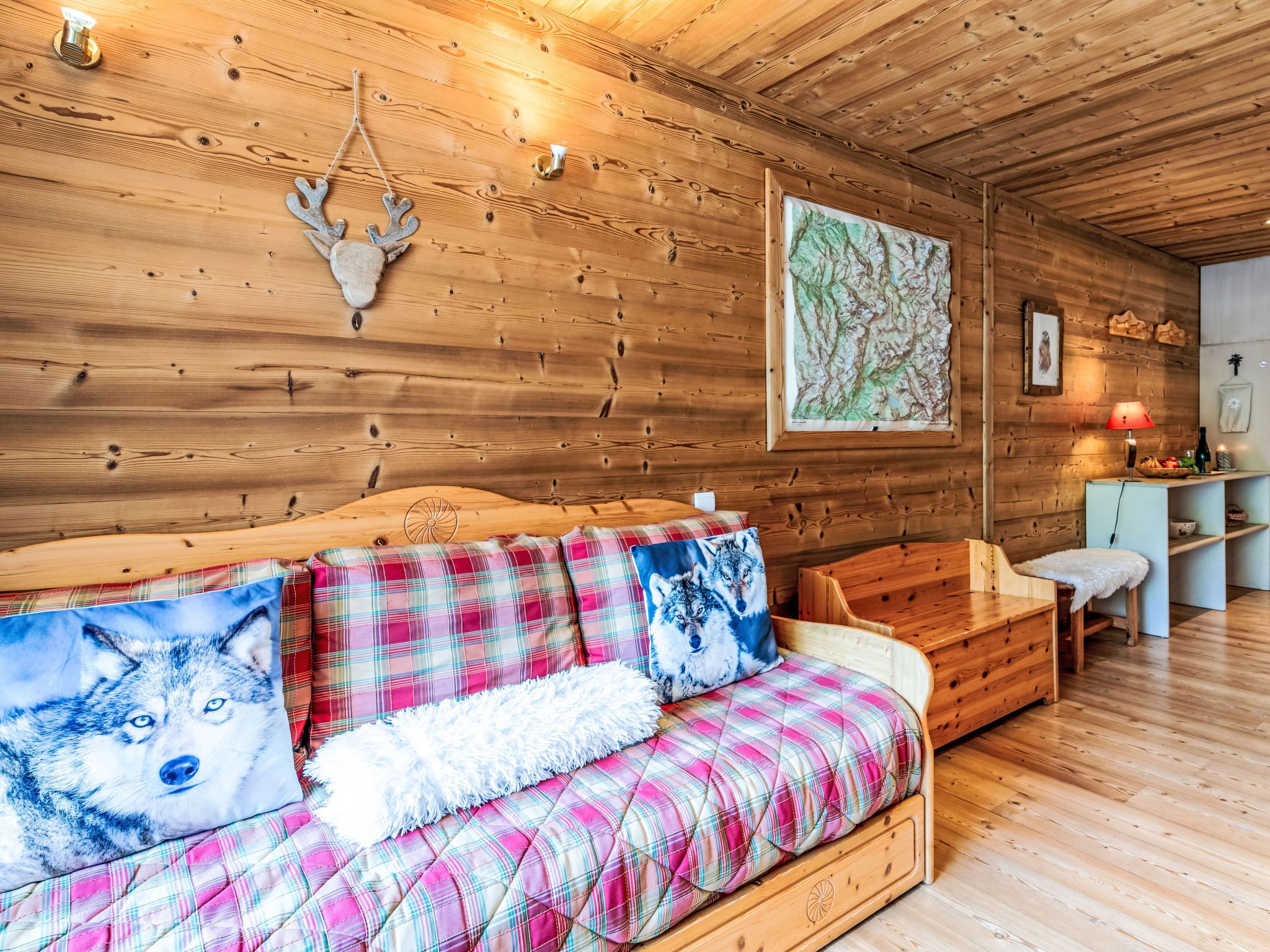 L’intérieur d’un chalet chaleureux, avec un mur en bois, un canapé agrémenté de coussins à carreaux, un banc en bois et une carte accrochée au mur.