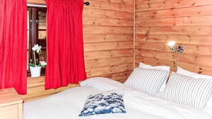 Una stanza con rivestimenti in legno, un letto, tende rosse, una pianta in vaso e una lampada da comodino.