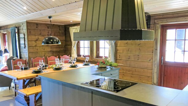 Una cucina moderna con rivestimenti in legno, un'isola centrale dotata di piano cottura e un'area pranzo con sedie e tavoli.