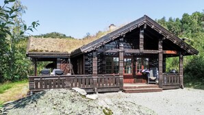 Un'accogliente baita di legno con veranda, un'area salotto esterna coperta e un grande masso in primo piano.