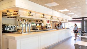 A modern bar area with a long counter, multiple beverage dispensers, and a coffee machine.