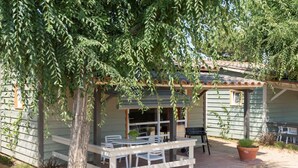 A rustic outdoor seating area with a wooden table and chairs, a potted plant, and a covered patio.