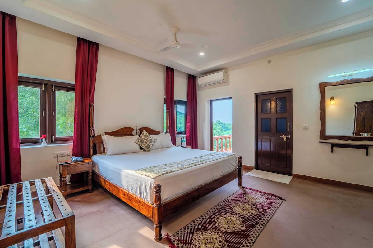 A bedroom with a large bed, a wooden nightstand, a small table, a patterned rug, and a large mirror on the wall.
