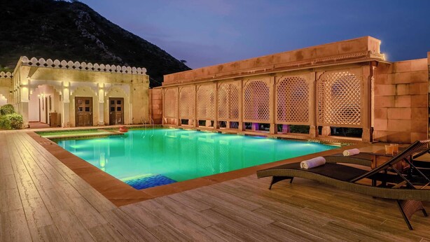 Un espace piscine doté d’une terrasse en bois, de chaises longues et d’un bâtiment aux fenêtres ornées de motifs en treillis.