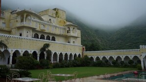 Un bâtiment traditionnel dot é de nombreux balcons et d’arcades, un espace piscine avec des tables et des chaises, et un jardin luxuriant.