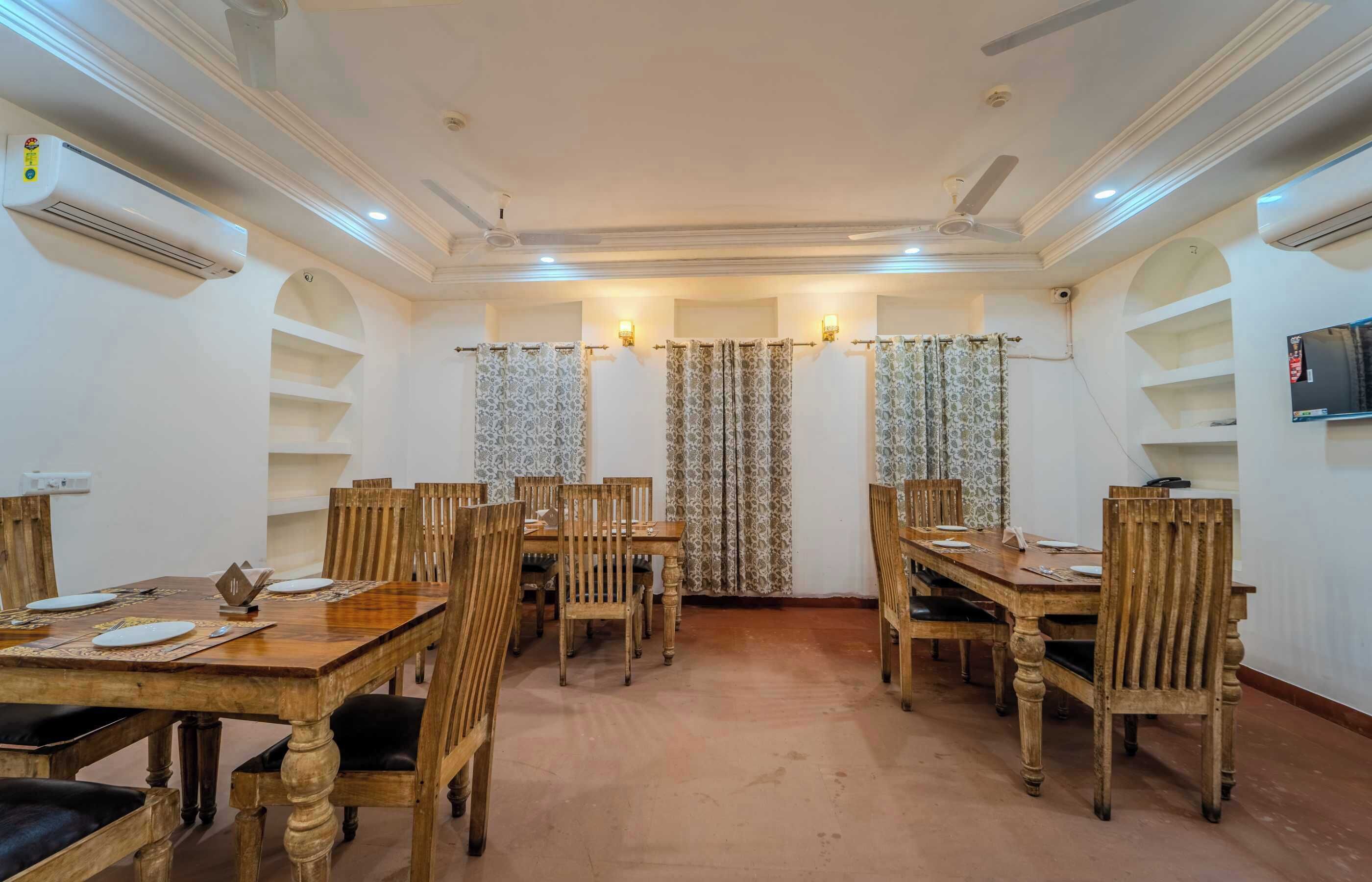 A dining area with wooden tables and chairs, air conditioning units, and a television on the wall.