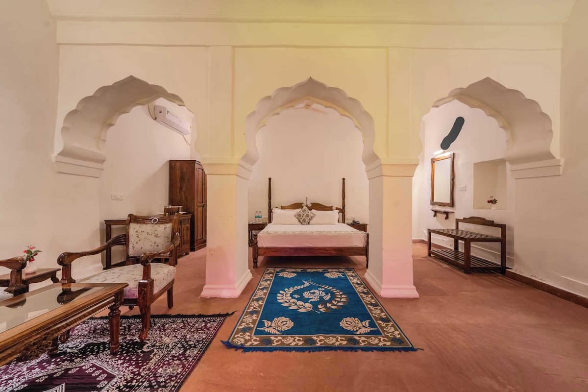 A room with a bed, two chairs, a small table, and a mirror.