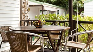 A patio with wicker chairs and a table, a decorative bowl with fruits, and a view of a row of houses in the background.