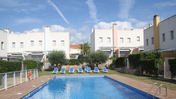 A rectangular swimming pool with a tiled edge, surrounded by a low brick wall. There are several blue lounge chairs aligned along the pool's edge. - Nice apartment with private terrace (Creixell)