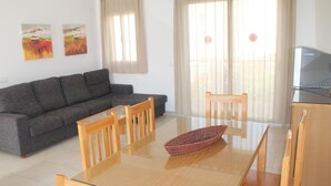 A living room with a grey sofa, wooden chairs, a glass dining table, and a TV on a wooden cabinet. - Nice apartment with private terrace (Creixell)