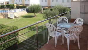 A balcony with a glass railing overlooking a courtyard with a pool, surrounded by greenery and white buildings. - Nice apartment with private terrace (Creixell)