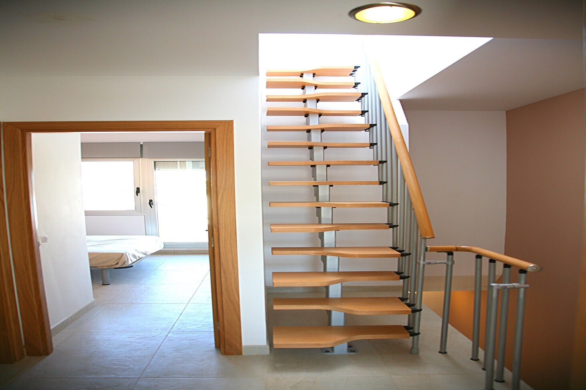 A staircase with wooden steps and metal railings, leading to a room with a bed and a window.