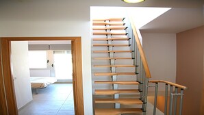 A staircase with wooden steps and metal railings, leading to a room with a bed and a window.