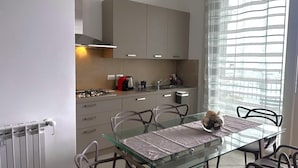 Una cucina moderna con un tavolo da pranzo in vetro, mobili grigi e una finestra con tende leggere.