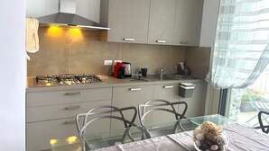 Una cucina moderna con piano cottura a gas, macchina da caffè e lavello. Ci sono pensili sopra al bancone e una finestra con tende.