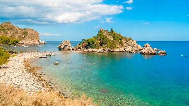 Paesaggio costiero con acque cristalline turchesi, formazioni rocciose e una spiaggia sabbiosa.