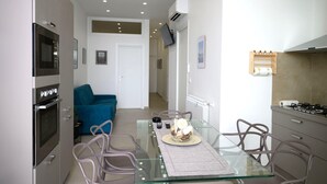 Una cucina moderna con un tavolo da pranzo in vetro, sedie e un divano blu sullo sfondo.