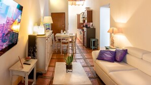 A cozy living room with a white sofa, a small table with a plant, and a dining area with a wooden table and chairs. - Il Castellare, a delightful apartment in the heart of Sierna (Siena)