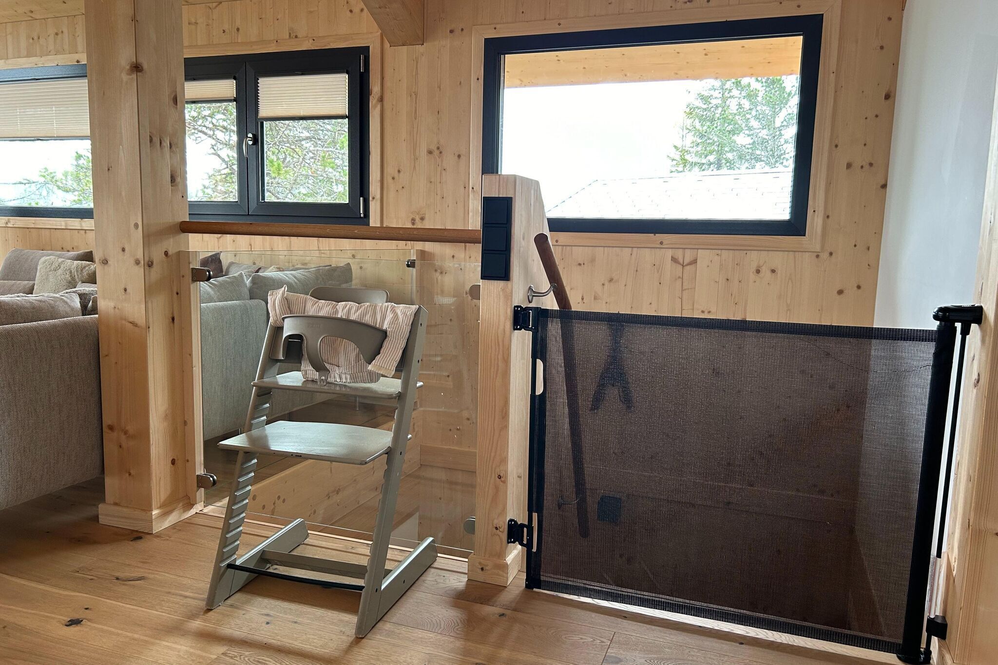 Un interior de madera con un sofá, una silla y una ventana con vistas a árboles.