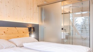 A modern bedroom with a wooden headboard, a glass shower enclosure, and a view of the outdoors. - Appealing chalet with finnish sauna (Turrach)