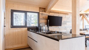 A modern kitchen with wooden walls, a large window, and a flat-screen TV. - Appealing chalet with finnish sauna (Turrach)