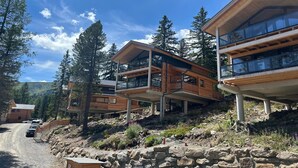 A modern multi-story building with large windows and wooden exterior, situated in a mountainous area with trees and a gravel road. - Appealing chalet with finnish sauna (Turrach)