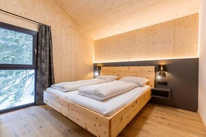 A wooden bedroom with a large bed, two bedside tables, and a window with curtains.