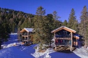 Dues cabanes de fusta amb grans finestres, envoltades de neu i arbres.