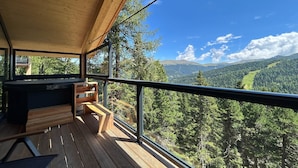 A wooden deck with a hot tub and seating, overlooking a forested valley. - Awesome chalet with sauna (Turrach)