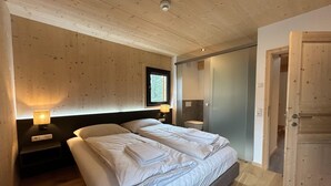 Quarto com duas camas, paredes de madeira, uma janela, abajures e uma porta.