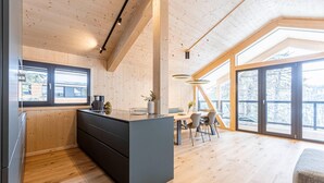 A modern kitchen with wooden walls and a large island, a dining area with natural light, and a view of the outdoors.