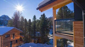 A wooden cabin with a balcony overlooking a snowy forest and mountains.