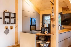 A modern kitchen with wooden cabinets, a built-in coffee machine, and a large TV. - Cozy chalet with sauna (Turrach)