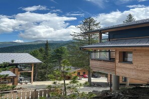 A modern wooden cabin with a balcony, surrounded by pine trees and a mountain view. - Lush chalet with indoor sauna (Turrach)
