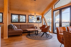 Un salon chaleureux avec un plafond en bois, de grandes fenêtres, un canapé, des fauteuils et une table basse.