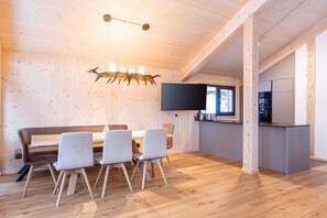 A modern kitchen with a flat-screen TV, wooden flooring, and a dining area with a bench and chairs.