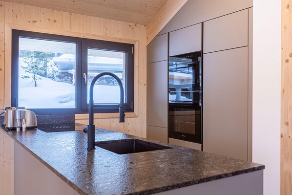 Cozinha moderna com bancadas de granito, eletrodomésticos de aço inoxidável e janela com vista para uma paisagem coberta de neve.