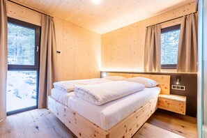 A wooden cabin bedroom with a bed, bedside table, and a window with curtains. - Inviting chalet with indoor sauna (Turrach)