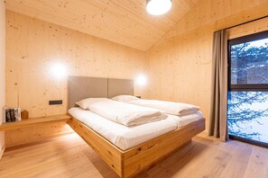 Un dormitorio de madera con cama, mesita de noche y ventana con vistas a árboles.