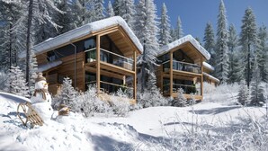 A modern wooden cabin with a balcony, surrounded by snow-covered trees. - Superior chalet withsauna & hottub (Turrach)