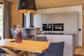A modern kitchen with integrated appliances, a dining area with a wooden table and chairs, and a pendant light fixture. - Superior chalet withsauna & hottub (Turrach)