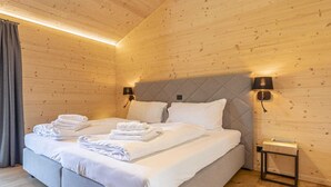 A neatly made bed with white linens and towels, two wall-mounted lamps, and a small bedside table with a book. - Superior chalet withsauna & hottub (Turrach)
