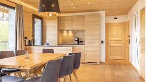 A modern kitchen with wooden cabinets, a central island, and a dining area with a wooden table and chairs. - Superior chalet withsauna & hottub (Turrach)