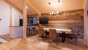 A modern kitchen with a wooden ceiling, a dining area with a long table and chairs, and a TV mounted on the wall. - Lavish chalet with sauna (Turrach)