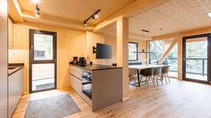 Eine moderne Küche mit Holzwänden und einer zentralen Kochinsel, ein Essbereich mit Tisch und Stühlen sowie große Fenster mit Blick ins Freie.