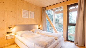 Ein Schlafzimmer einer Holzhütte mit zwei Betten, einem Fenster mit Vorhängen und einem Nachttisch mit Lampe.
