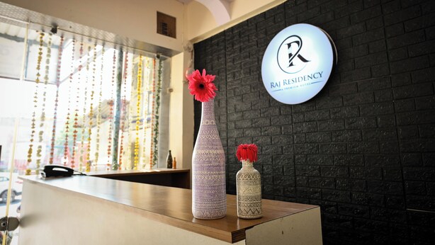 A reception desk with two vases, one with a red flower and another with a red pom-pom, and a sign reading "RAJ RESIDENCY". - Raj Residency (Jodhpur)