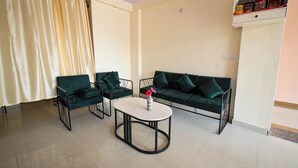 A living room with a green sofa, two armchairs, a round coffee table, and a curtain. - Raj Residency (Jodhpur)
