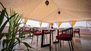 A covered outdoor dining area with tables and chairs, a view of the cityscape, and a decorative ceiling. - Raj Residency (Jodhpur)