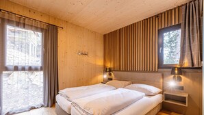 A room with two beds, wooden walls, a window with curtains, and wall-mounted lamps. - Lavish chalet with sauna & hot tub (Turrach)